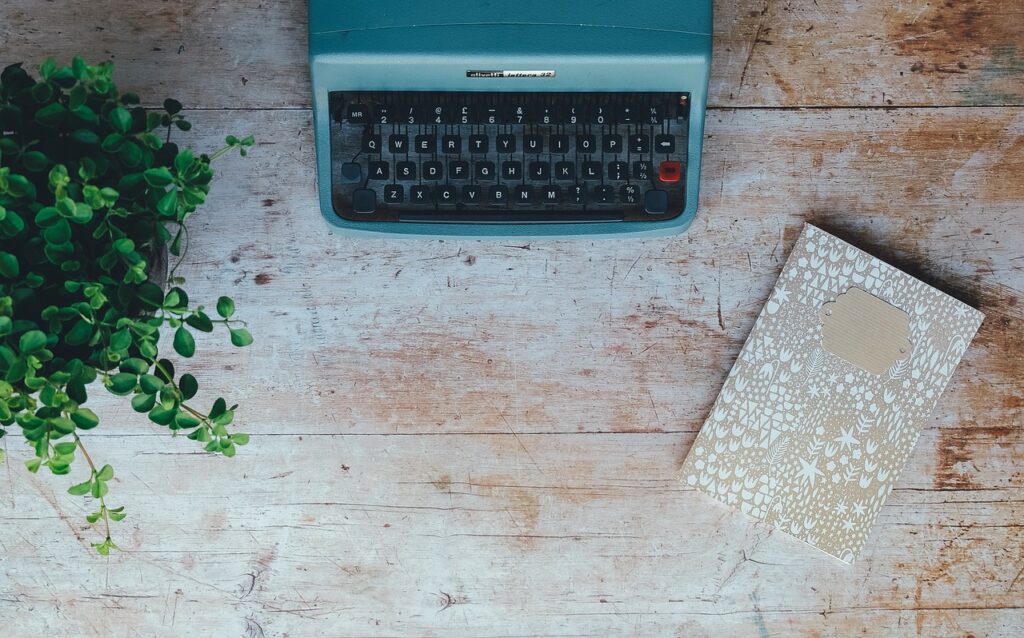 Bird's eye view of vintage typewriter, plant and notebook on desk