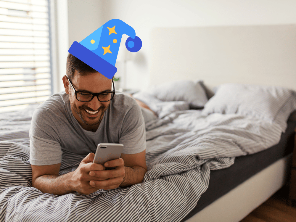 Man smiling in bed while reading emails on his phone